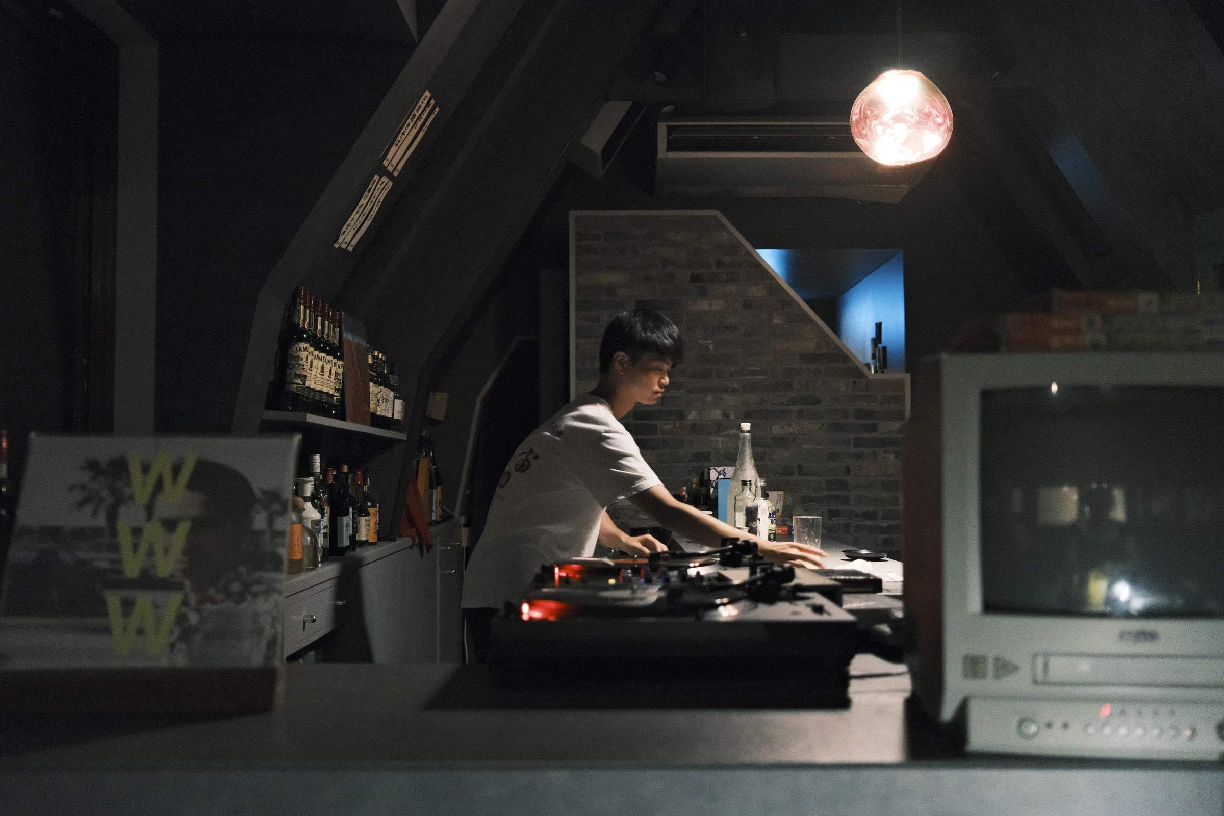 Bartender at MUSIC BAR universe changing the music on a record player, in a dimly-lit record bar in Kyoto