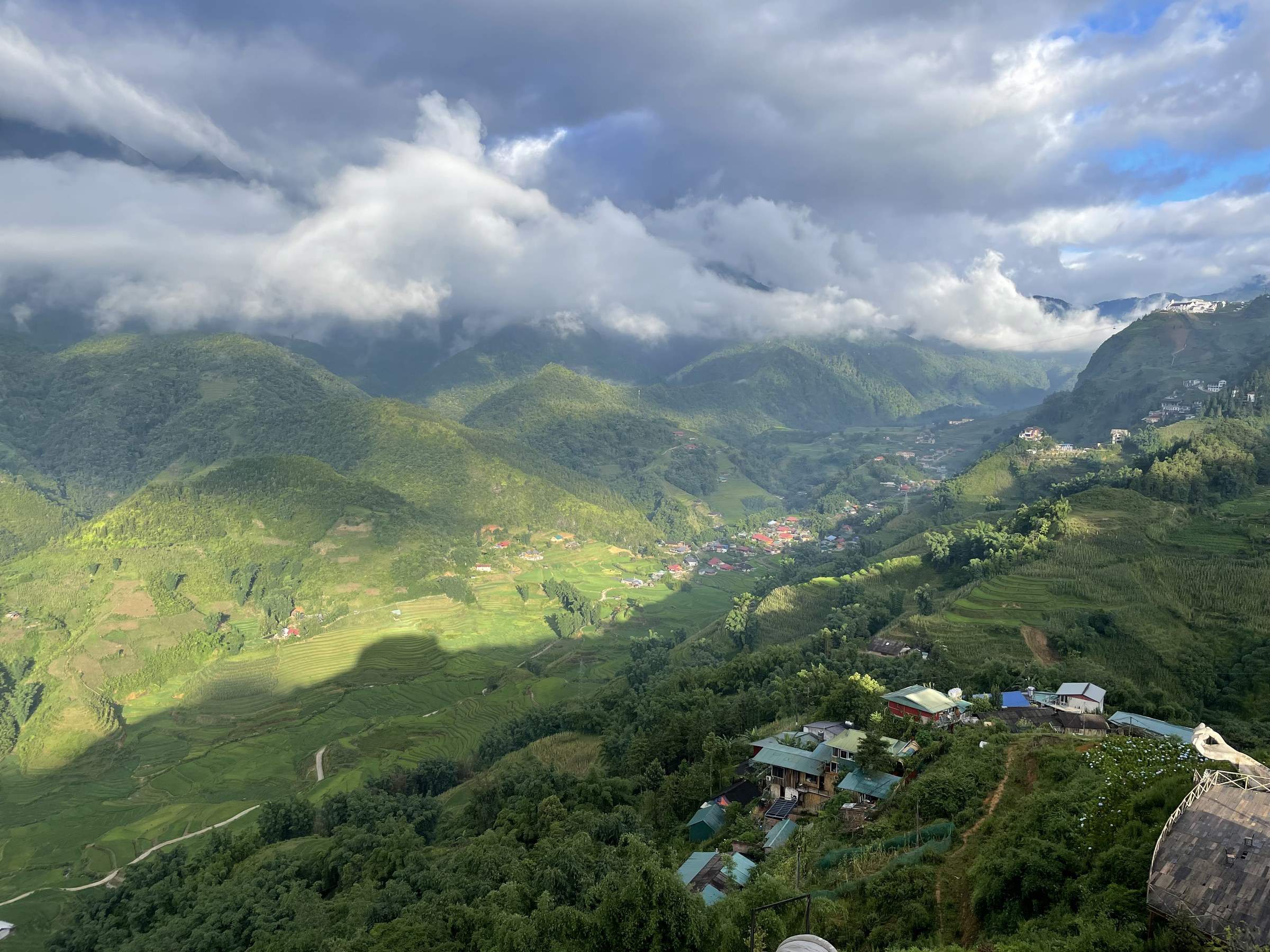 A breathtaking view of lush, green mountains in Sapa, Vietnam under a dramatic, cloudy sky, with a small village nestled in a valley, showcasing the serene beauty of nature.