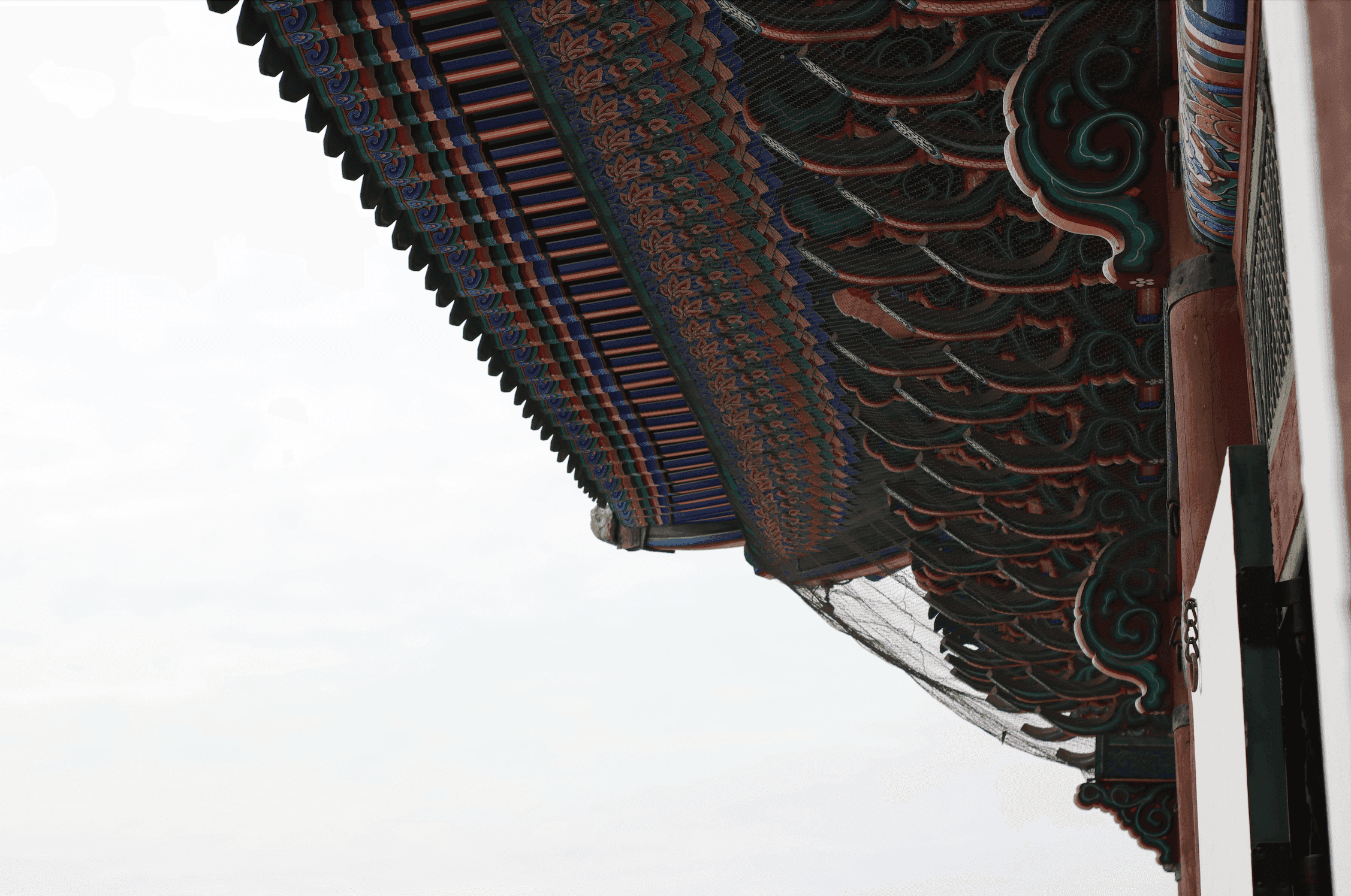 A close-up of a Gwanghwamun palace's eave with intricate details against a white sky background