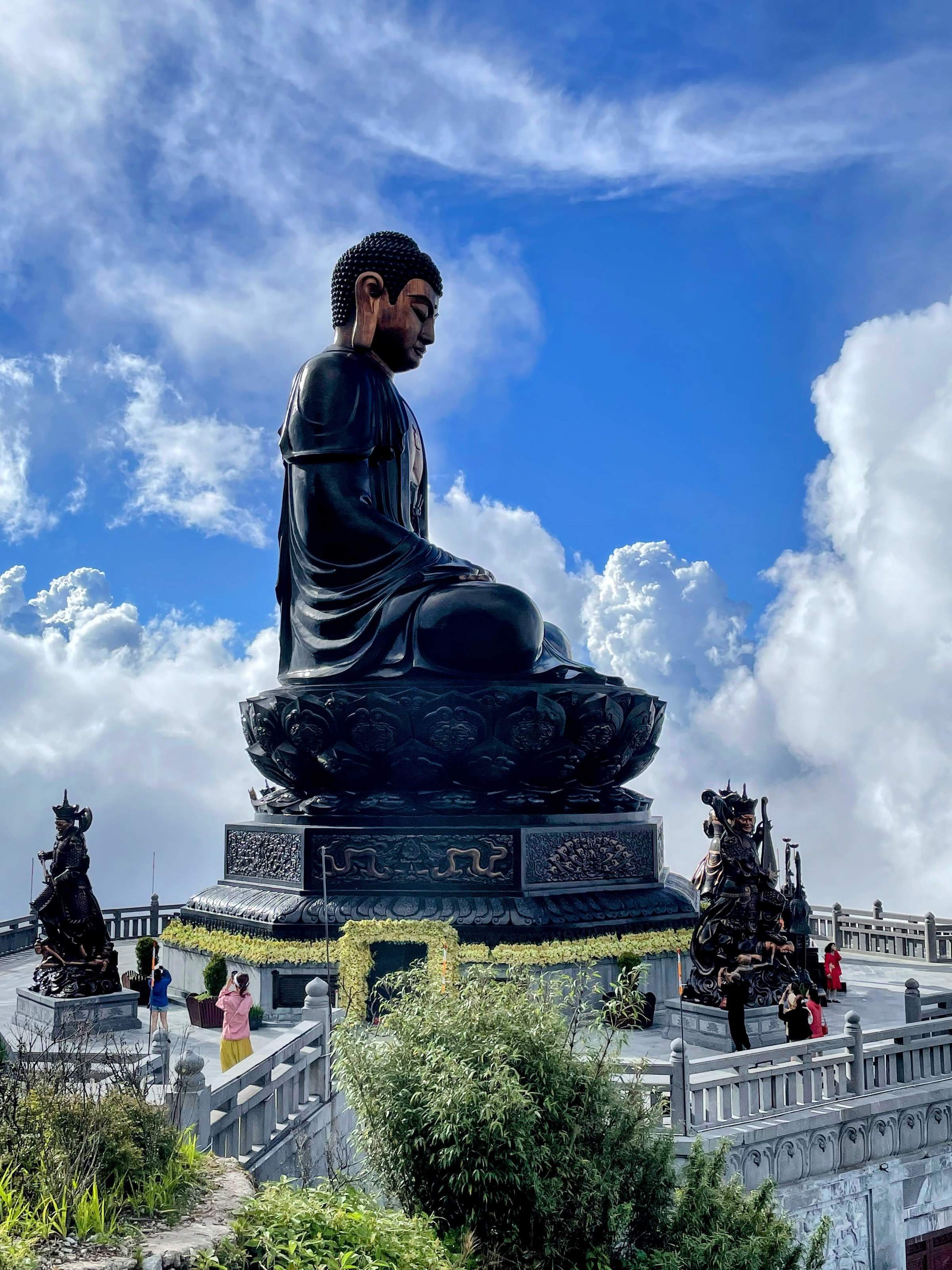A large Buddha statue sits serenely against a backdrop of blue skies and wispy clouds on Fansipan Mountain in Vietnam